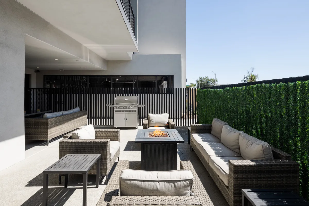 An outdoor social hub featuring a fire pit surrounded by comfortable seating, a BBQ grill, and lush greenery. The ambiance suggests evenings spent dining, socializing, and unwinding under the Arizona night sky.