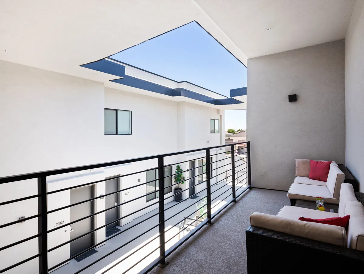 This image captures a modern balcony with comfortable seating, open sky views, and sleek railings. The inviting setting is suited for morning coffees, reading outdoors, or watching the city wind down at dusk. The mood is serene, with a touch of sophistication, reinforcing the idea of indoor-outdoor living.
