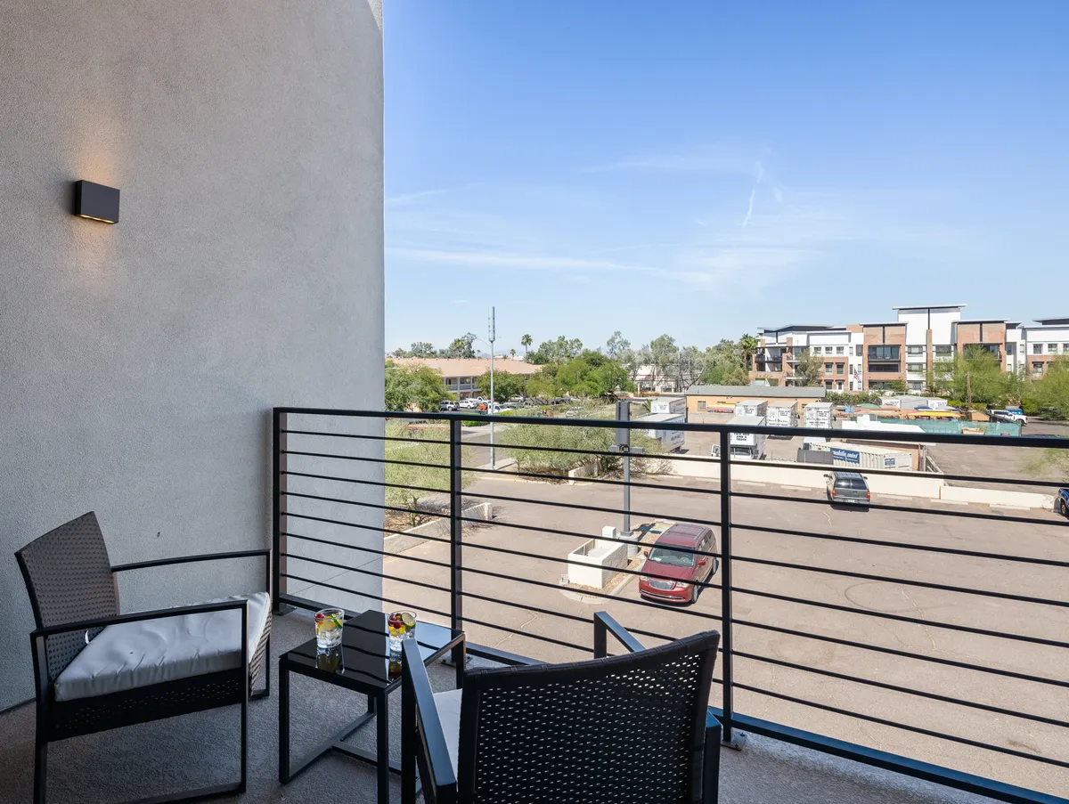 This image features a welcoming balcony with comfortable seating and a small table, offering a view of the surrounding area. The setup invites guests to enjoy fresh air and take in the neighborhood sights, suggesting relaxation and connection to the outdoors.