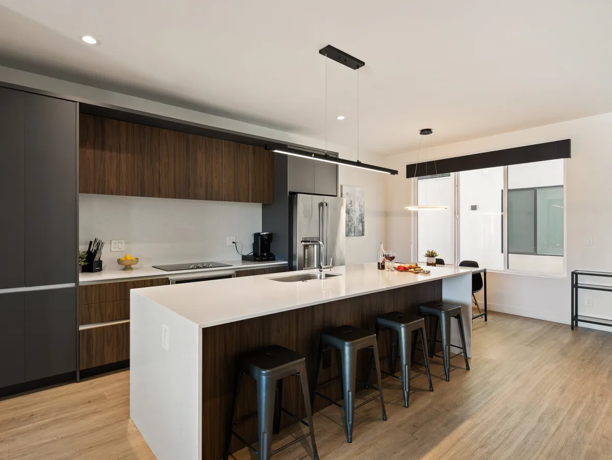 A well-lit kitchen with a large island that includes bar stools, high-end appliances, and a window view. The scene suggests the space is ready for cooking, entertaining, and gathering, emphasizing the kitchen’s role as a social hub.