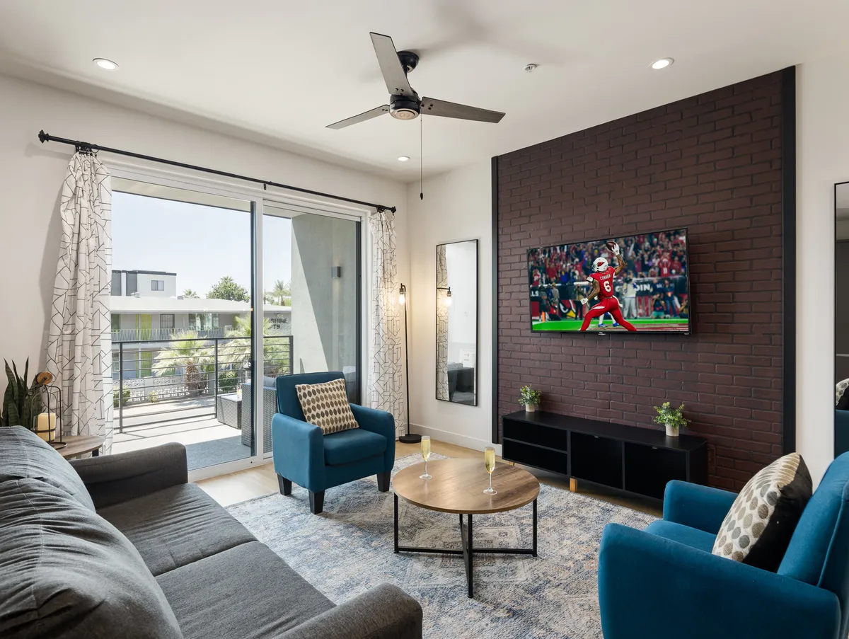 A cozy lounge area with plush blue armchairs, a coffee table, and a television tuned to a sports event. The setup invites relaxed conversations, streaming, and communal gatherings.