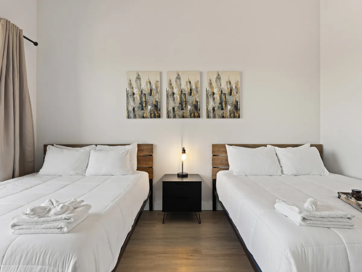 A cozy bedroom featuring two beds with crisp white linens, a black nightstand between them, and modern wall art. The setup is ideal for families or groups, with a relaxed and welcoming vibe.