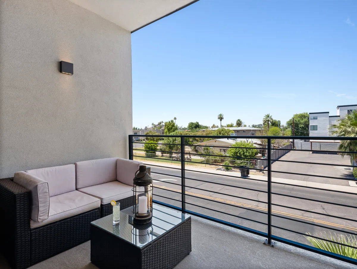 A furnished balcony with comfortable seating and a glass table overlooking the street, inviting guests to relax and enjoy the view. The setting is ideal for morning coffee, evening drinks, or simply soaking up the urban atmosphere.