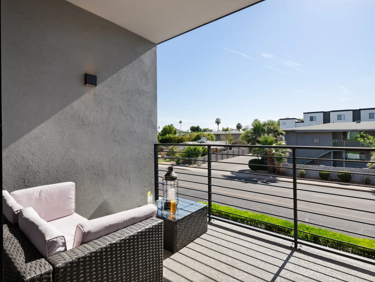 This image shows a serene balcony with comfortable seating, a decorative lantern, and a view of the street below. The scene captures the sense of relaxing outdoors, whether enjoying the morning light or watching the sunset. The setting suggests an inviting space to unwind and take in the energy of the surrounding neighborhood.